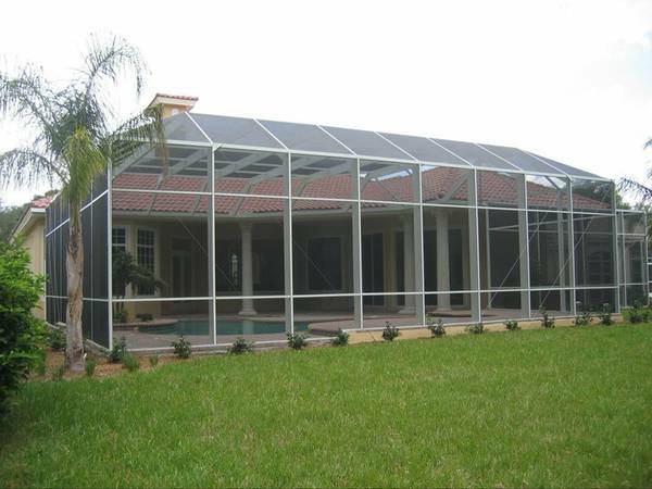 Screen enclosure covers a pool and columned lanai in front of a tile-roof stucco house.