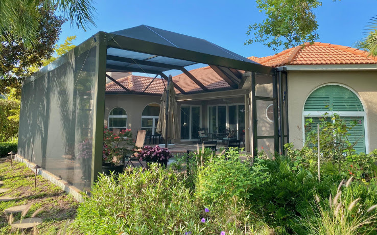 Screen enclosure attached to a tile-roof stucco house, with dense landscaping in the foreground.