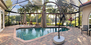 Screened paver lanai with a market umbrella beside a pool, a lake visible beyond the screen.