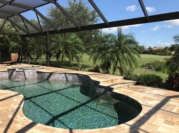 Freeform pool with a rock waterfall spa sits inside a screen enclosure overlooking a golf course.