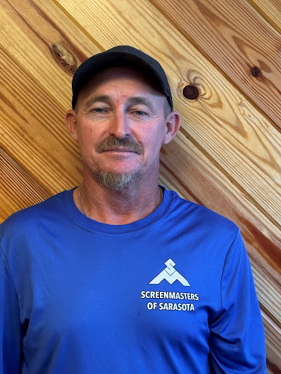 Screenmasters team member in a blue branded shirt, portrait against a wood-plank backdrop.