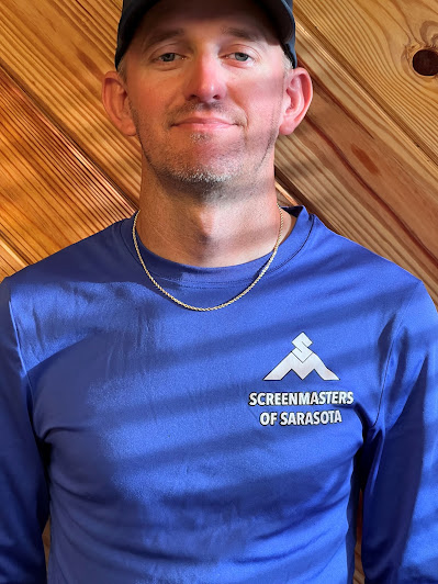 Screenmasters team member in a blue branded long-sleeve shirt, portrait against a wood-plank backdrop.